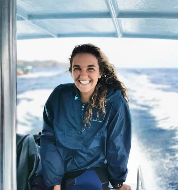Mujer sonriendo sentada en la proa de una lancha en movimiento rumbo a Nusa Lembongan, con agua y estela detrás.