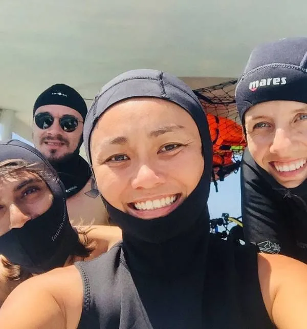 Cuatro buceadores sonriendo en traje y capucha neopreno en un barco antes de una inmersión cerca de Nusa Lembongan.