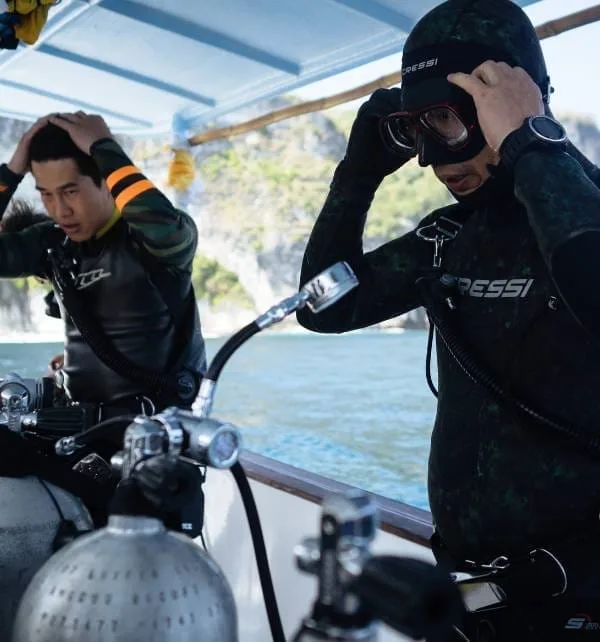 Dos buceadores en Nusa Lembongan ajustan sus máscaras y equipos de inmersión en la cubierta de una embarcación antes de zambullirse.